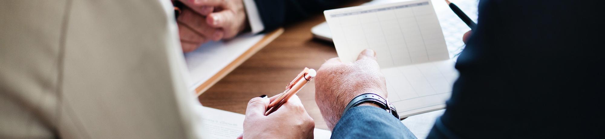 people with pen poised at a conference table